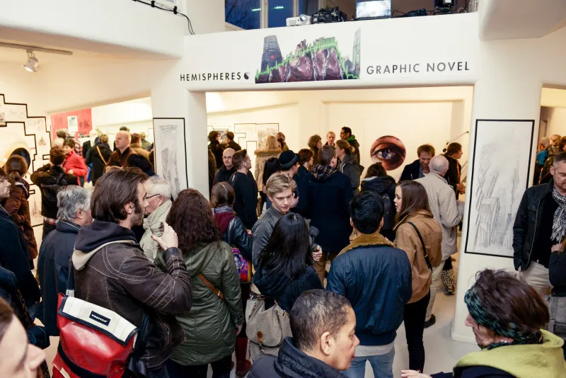 Volle Ausstellungsräume, an den Wänden gerahmte Comicseiten, über dem Durchgang der Schriftzug „Hemispheres Graphic Novel“.